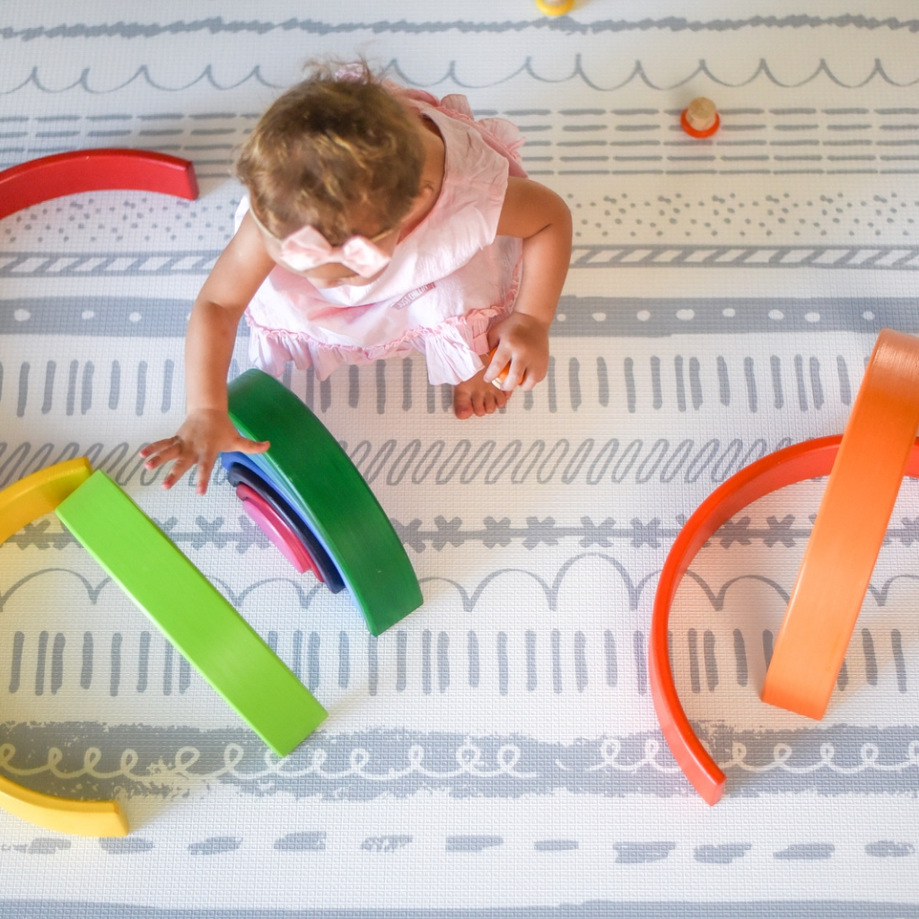 A little girl sitting on the floor with Bumboo Kids' Animal Alphabet/Boho play mat.