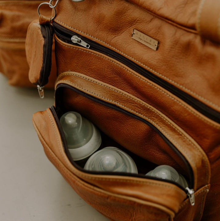 Brown leather bag with baby bottles inside on a light background