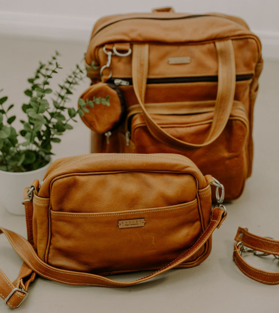 Two brown leather bags on a light surface with a plant in the background