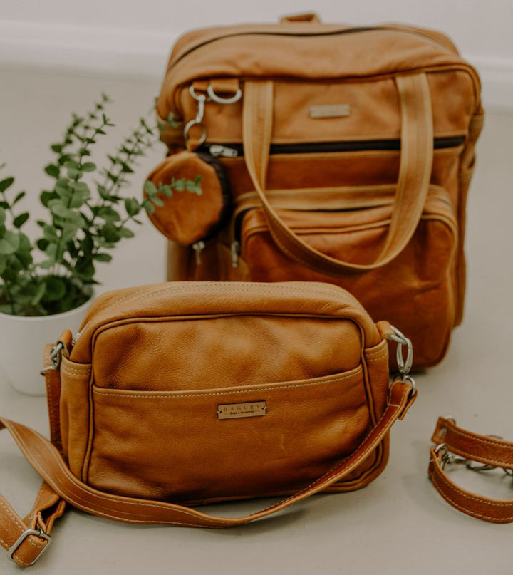 Two brown leather bags on a light surface with a plant in the background