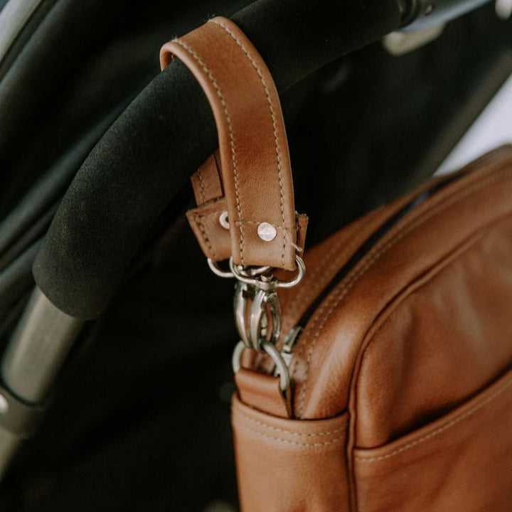 Brown leather bag with a pram strap attached to a stroller handle