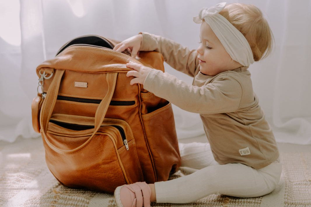 Child interacting with a brown leather bag on a checkered floor with white curtains in the background