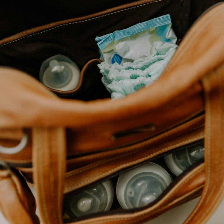 Brown leather bag with baby items including diapers and bottles on a neutral background
