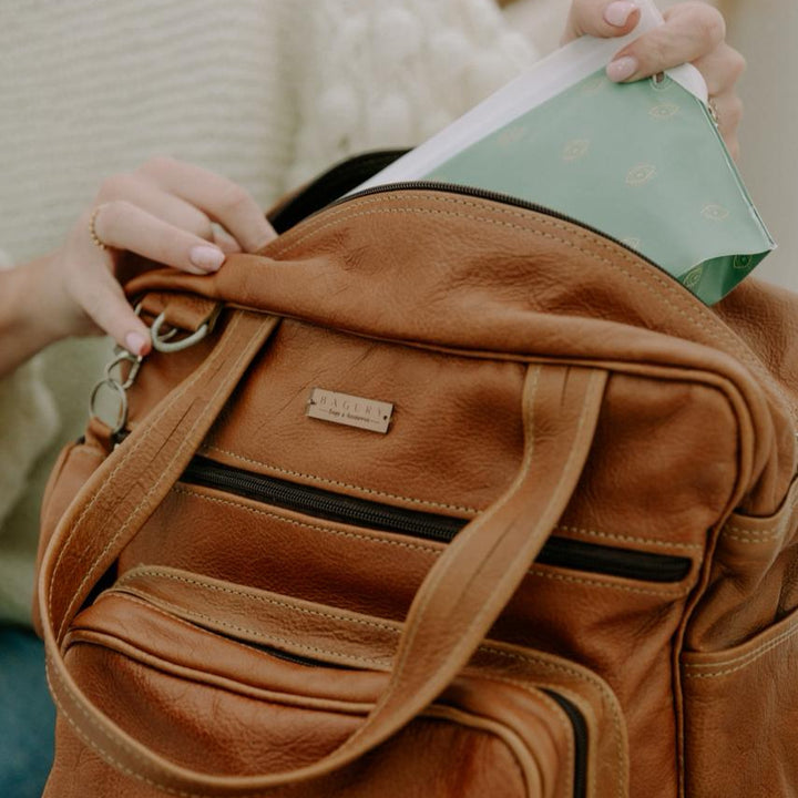 Brown leather bag with a visible brand logo, held by a person.