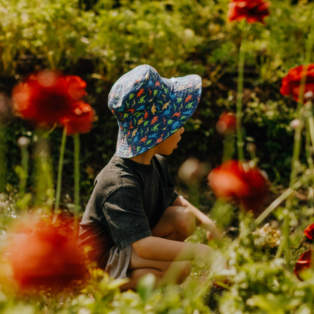 Child wearing a colorful sun hat sitting in a field of red flowers