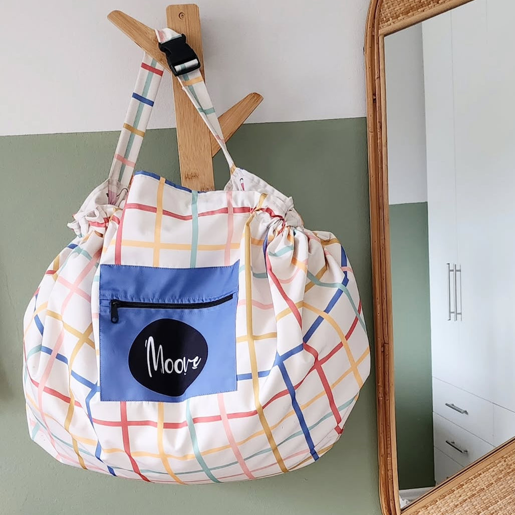 Multicolored drawstring bag with a blue pocket labeled moove hanging on a wooden hook.