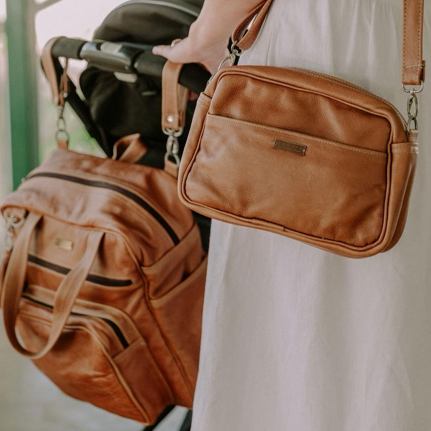 Person holding a brown leather bag with a stroller in the background