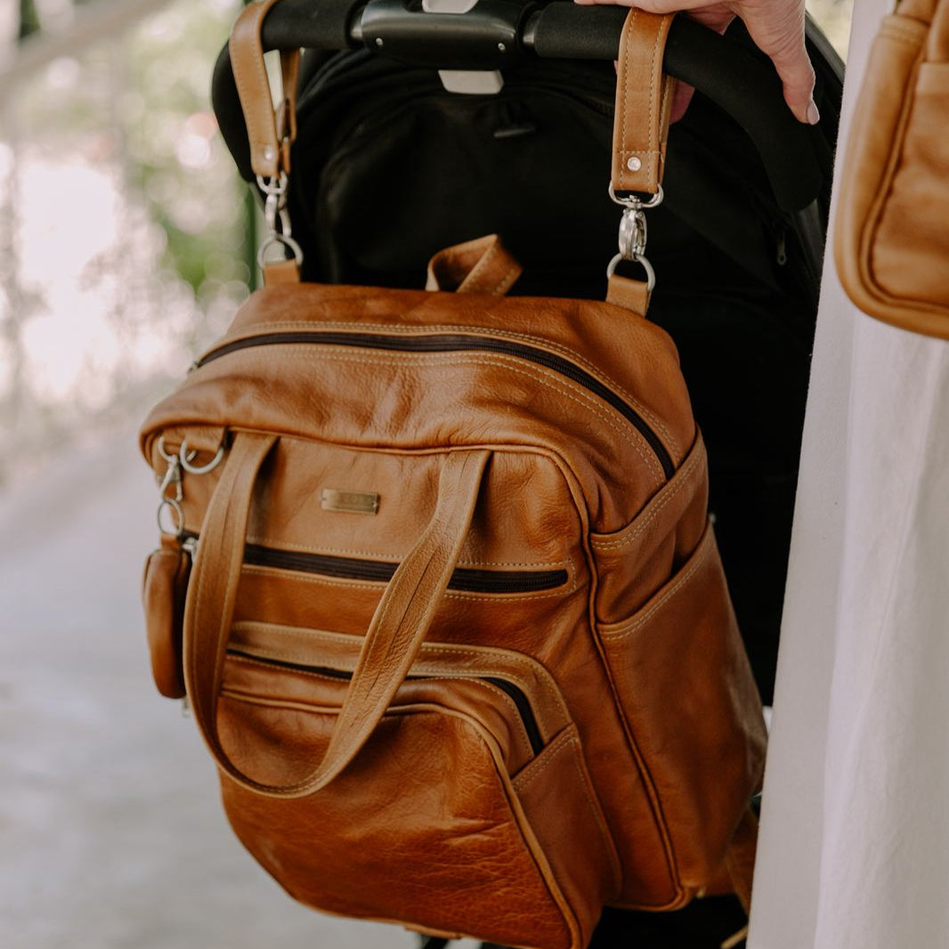 Brown leather backpack attached to a black stroller with a blurred background